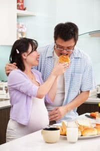 Pregnant person feeding partner in kitchen with counter full of food