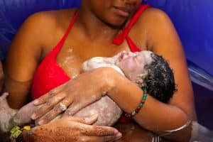 New parent in birth tub holding newborn baby just after birth