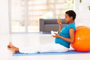 pregnant woman eating healthy salad on exercise mat