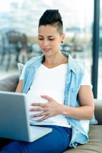 Pregnant person using laptop and holding pregnant belly